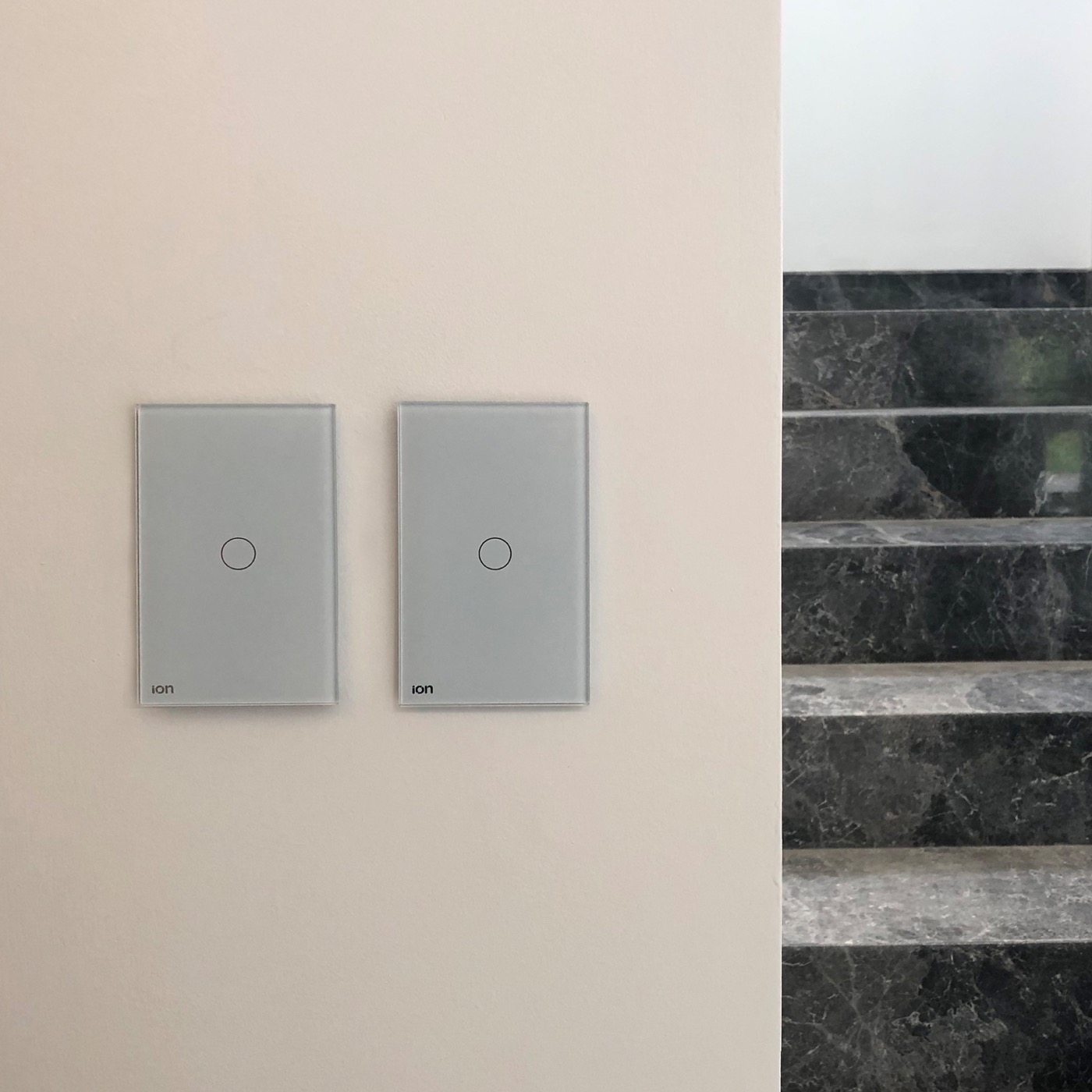 Interruptores ION Glass grises instalados en pared de travertino — residencia con escalera de mármol negro