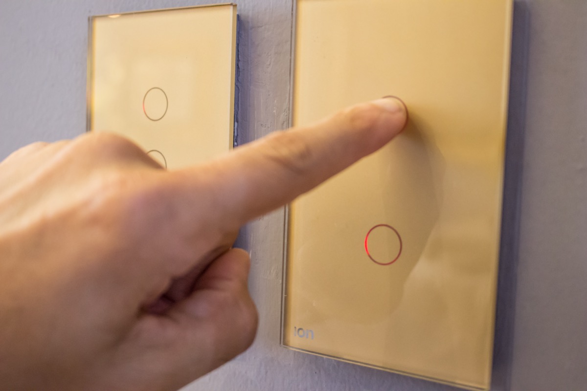 Mano presionando interruptor ION Glass dorado — experiencia touch con conectividad WiFi y app Tuya
